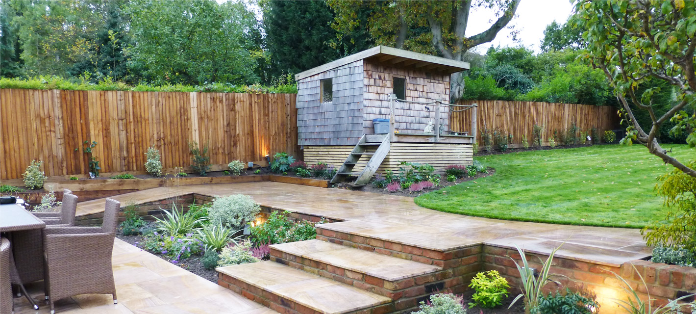 Sloped patio and steps leading up to a raised shed and gently curved lawn